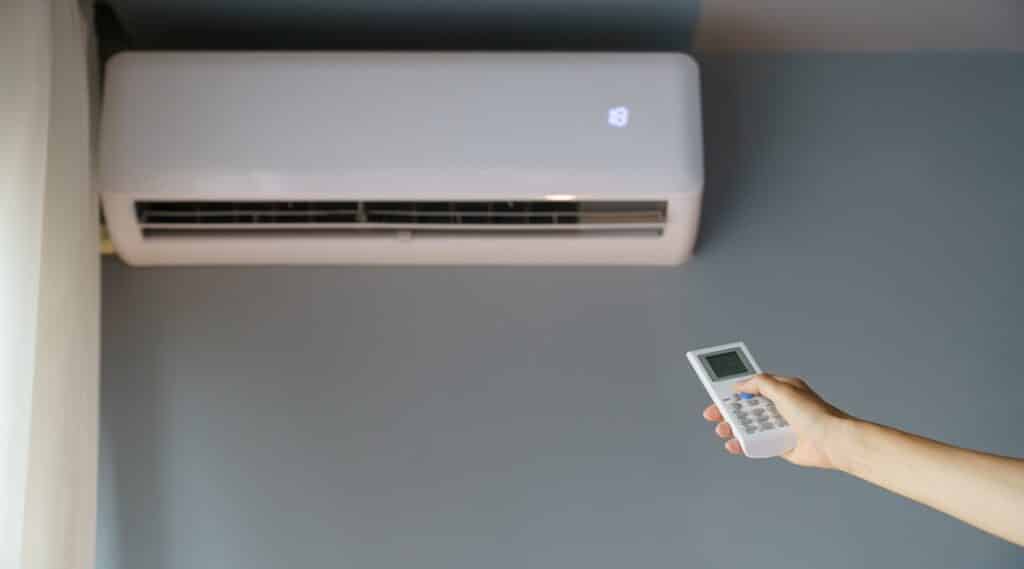 Owner turns on air conditioner hanging on wall with remote control to warm up cold apartment