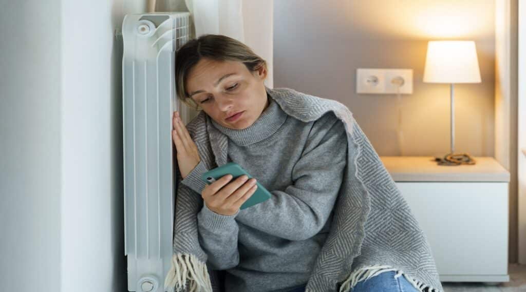 Young woman snuggling up to cold battery loses motivation and sense of living and scrolls phone