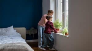 Attentive son kid boy doing household chores with mom taking care of green home plants. Family time.